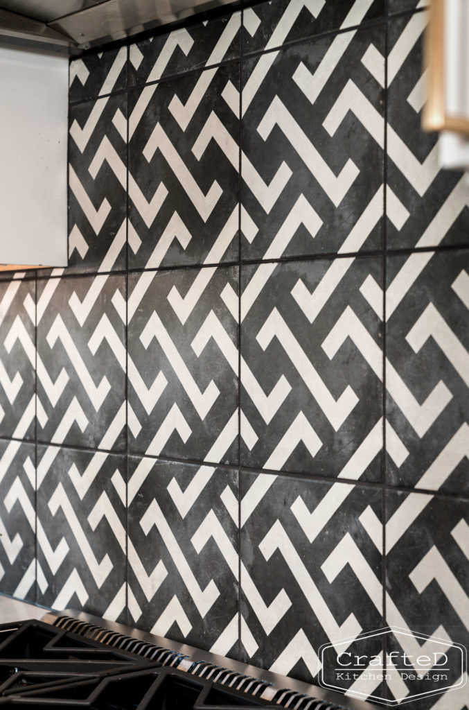 black and white patterned kitchen backsplash with black hood and white cabinets