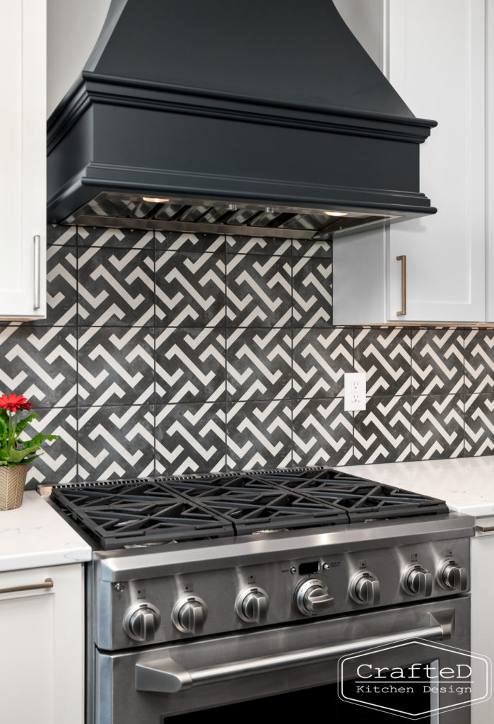 black and white patterned kitchen backsplash with black hood and white cabinets